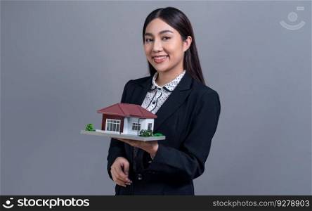 Confident Asian businesswoman holding house model, advertising home loan with smile. Real estate agent with s&le house model in hand on isolated background for business advertisements. Jubilant. Confident Asian businesswoman holding house model. Jubilant