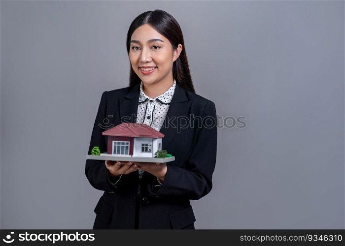 Confident Asian businesswoman holding house model, advertising home loan with smile. Real estate agent with sample house model in hand on isolated background for business advertisements. Jubilant. Confident Asian businesswoman holding house model. Jubilant