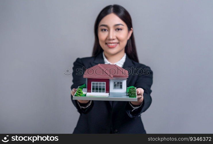 Confident Asian businesswoman holding house model, advertising home loan with smile. Real estate agent with s&le house model in hand on isolated background for business advertisements. Jubilant. Confident Asian businesswoman holding house model. Jubilant