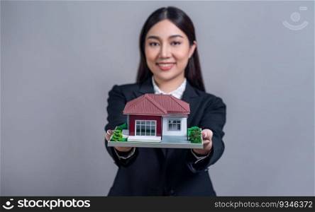 Confident Asian businesswoman holding house model, advertising home loan with smile. Real estate agent with s&le house model in hand on isolated background for business advertisements. Jubilant. Confident Asian businesswoman holding house model. Jubilant