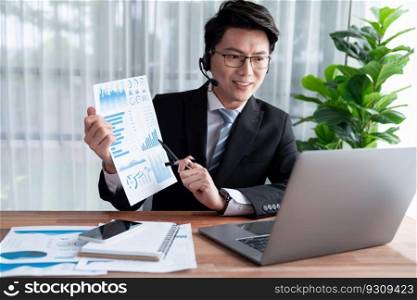 Confident asian telesales businessman work in modern office wearing headphone, presenting BI dashboard analysis to clients and customers in online meeting. Success modern telesales business . Jubilant. Asian telesales businessman work in office wearing headphone. Jubilant
