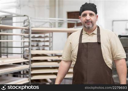 Confident baker posing with rack of fresh bread loaf at bakery. High quality photo. Confident baker posing with rack of fresh bread loaf at bakery.