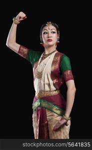 Confident Bharatanatyam dancer flexing muscle over black background