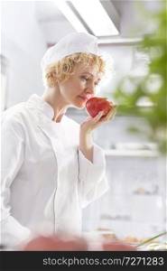 Confident blond chef smelling fresh red tomato in kitchen at restaurant