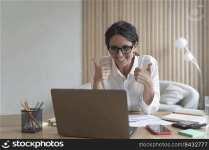 Confident business lady looking at  computer screen with broad smile while showing thumbs-up with both hands. Spanish female tutor working on laptop at home office. Remote work concept. Business lady looking at  computer screen with broad smile while showing thumbs-up with both hands