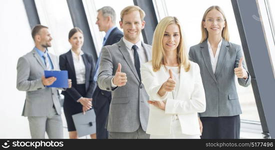 Confident business team. Confident business team showing thumbs up in office against the window