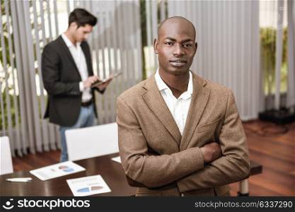 Confident businessman. Cheerful young African man in formalwear keeping arms crossed and smiling while his caucasian colleague standing on background