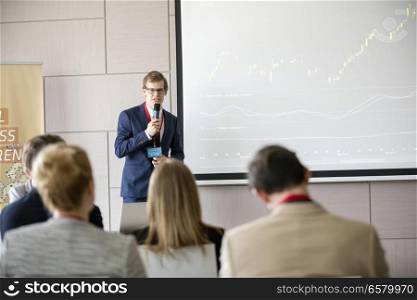 Confident businessman giving presentation in seminar hall at convention center