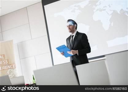 Confident businessman holding clipboard while standing in seminar hall