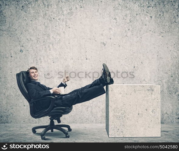 Confident businessman. Smiling businessman sitting in chair with legs on table