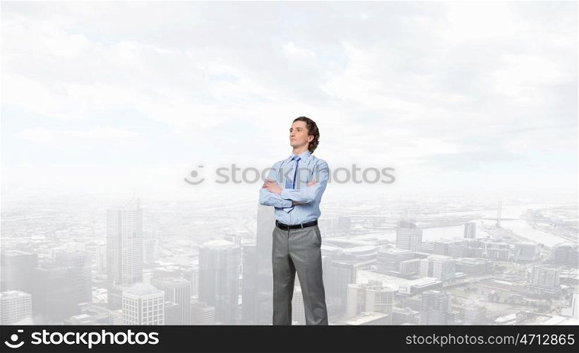 Confident businessman with arms crossed on chest against modern city view