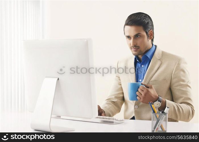 Confident businessman with coffee cup working on computer in office