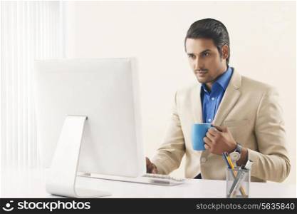 Confident businessman with coffee cup working on computer in office