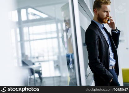 Confident businessman with ginger hair using mobile phone in modern office