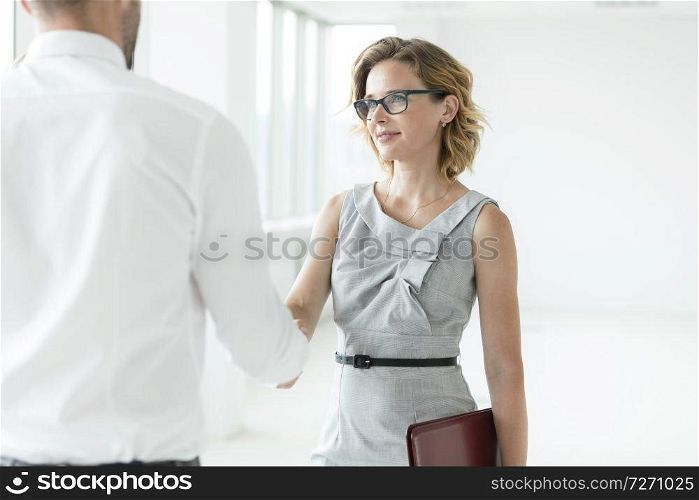 Confident businesswoman greeting businessman with handshake in new office
