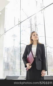 Confident businesswoman looking away while holding folder at office lobby