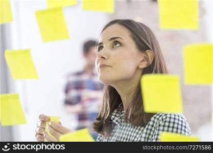 Confident businesswoman planning while looking at adhesive notes stuck on glass wall