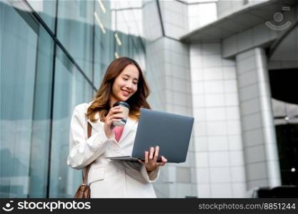 Confident businesswoman using computer laptop standing while drinking a cup of coffee takeaway at the city exterior. Beautiful smile female being ready to work. Business lifestyle concept.
