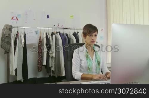 Confident businesswoman, young woman working as fashion designer, manager with computer in studio, talking on mobile phone. People, career, success, business, industry, busy worker in office