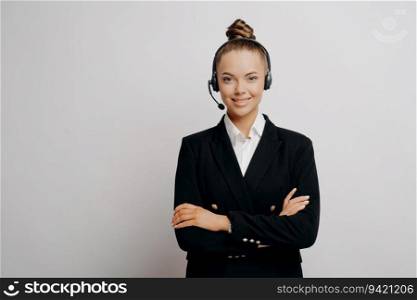 Confident call center manager in dark suit, arms crossed, overlooks workers in office, ready to work, light wall behind.