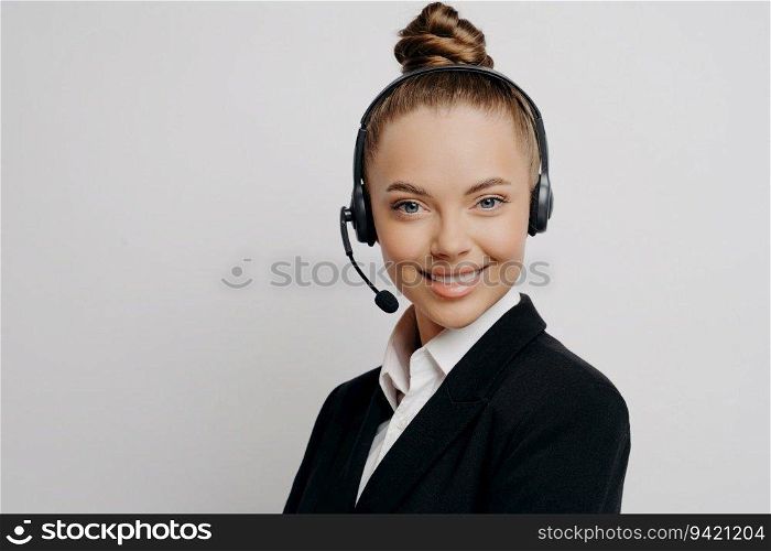 Confident call center manager in dark suit, headset, happily poses in office, having online call.