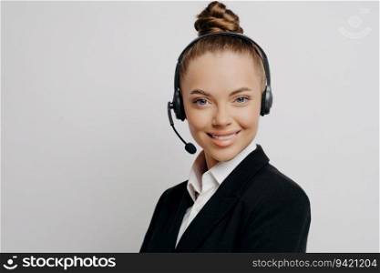 Confident call center manager in dark suit, headset, happily poses in office, having online call.