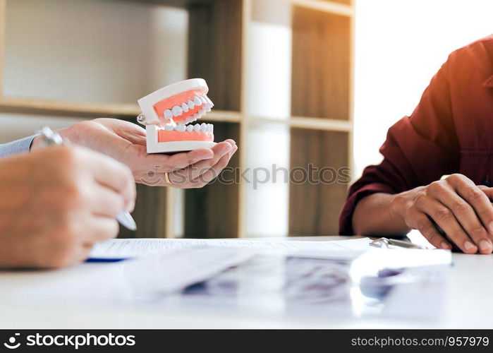 Confident dentist man holding a dentures with talking senior patient at office room.