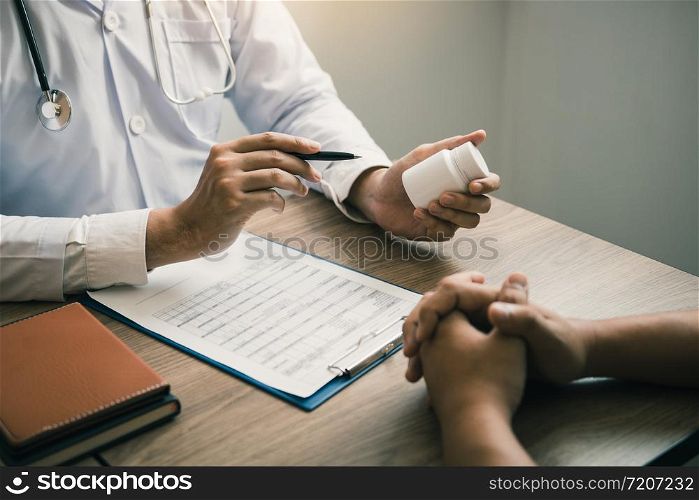 Confident doctor man holding a pill bottle and talking with senior patient and reviewing his medication at office room.