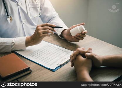 Confident doctor man holding a pill bottle and talking with senior patient and reviewing his medication at office room.