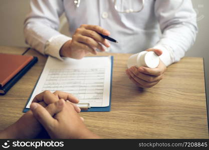 Confident doctor man holding a pill bottle and talking with senior patient and reviewing his medication at office room.