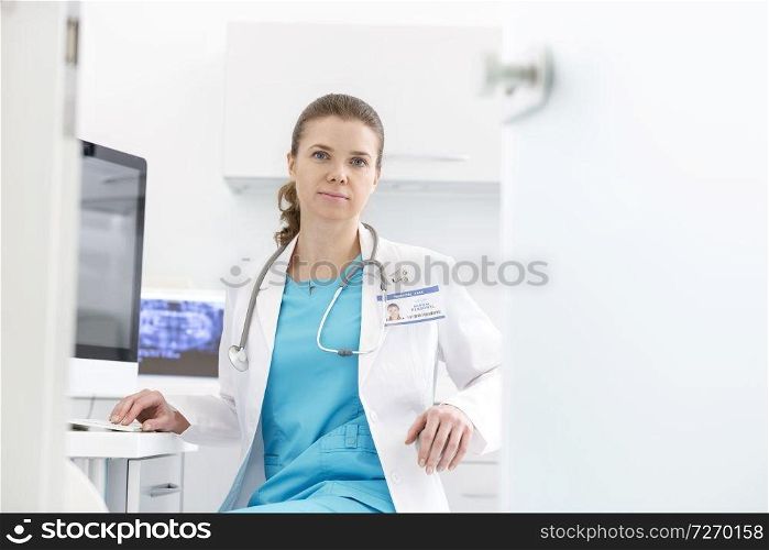 Confident doctor sitting at computer desk in dental clinic