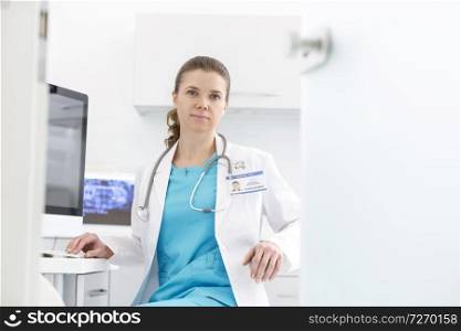 Confident doctor sitting at computer desk in dental clinic