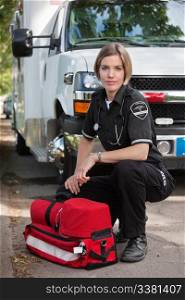 Confident EMS paramedic kneeling by portable oxygen unit and ambulance