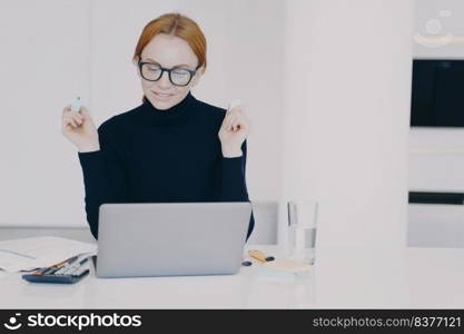 Confident female entrepreneur at work. Red haired woman in office is doing paperwork with marker pen and highlighting text. Positive caucasian girl entrepreneur is working on project at laptop.. Confident female entrepreneur woman in office is doing paperwork with marker pen highlighting text.