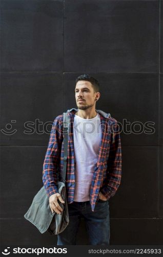 Confident handsome bearded male in jeans jacket posing for the camera against black wall