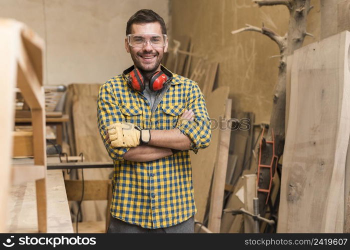 confident happy carpenter with his arm crossed standing workshop
