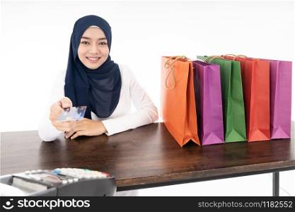 Confident happy smiling female muslim woman pay for her shopping with credit card with EDC machine using as consumerism and shopaholic concept. Studio shot on white background.