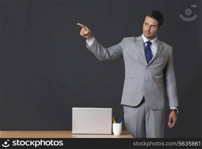 Confident Indian businessman pointing away while standing at office desk