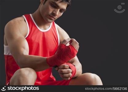 Confident male boxer taping up hands over black background