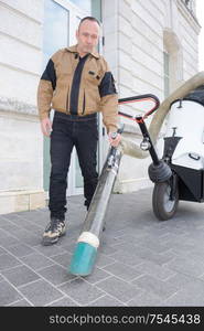 confident male janitor with vacuum cleaner on street