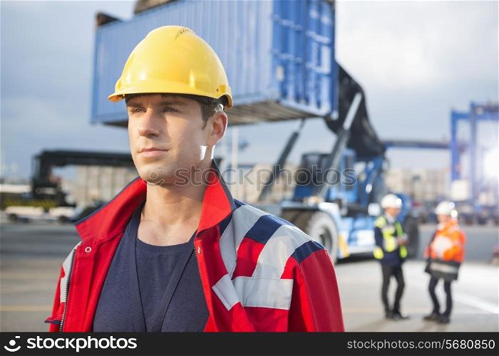 Confident male worker with colleagues in background at shipping yard