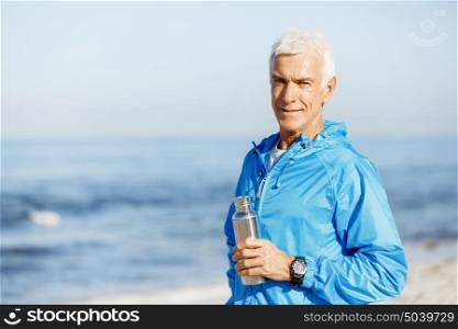 Confident man holding bottle with water . Confident man in sport wear holding bottle with water