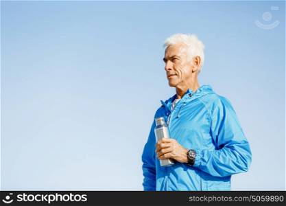 Confident man holding bottle with water . Confident man in sport wear holding bottle with water