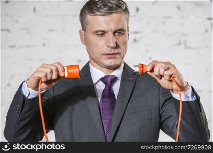 Confident mature businessman attaching red cables against white brick wall