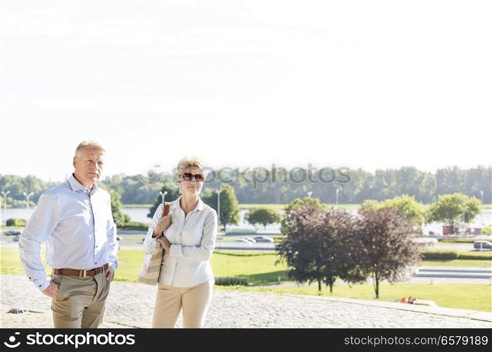 Confident middle-aged couple standing at park against clear sky