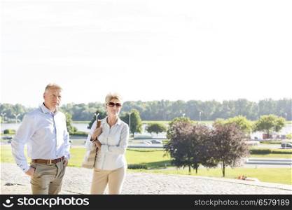Confident middle-aged couple standing at park against clear sky