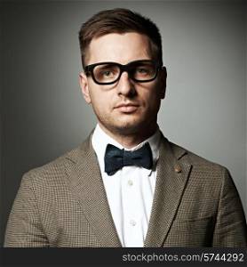Confident nerd in eyeglasses and bow tie against grey background