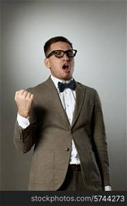 Confident nerd in eyeglasses and bow tie enjoying success against grey background