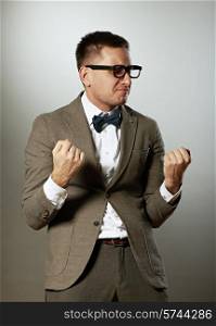 Confident nerd in eyeglasses and bow tie enjoying success against grey background
