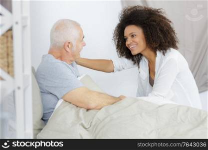 confident nurse with senior man lying on bed